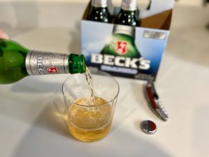 pouring becks non alcoholic beer into a glass with the 6 pack in the background